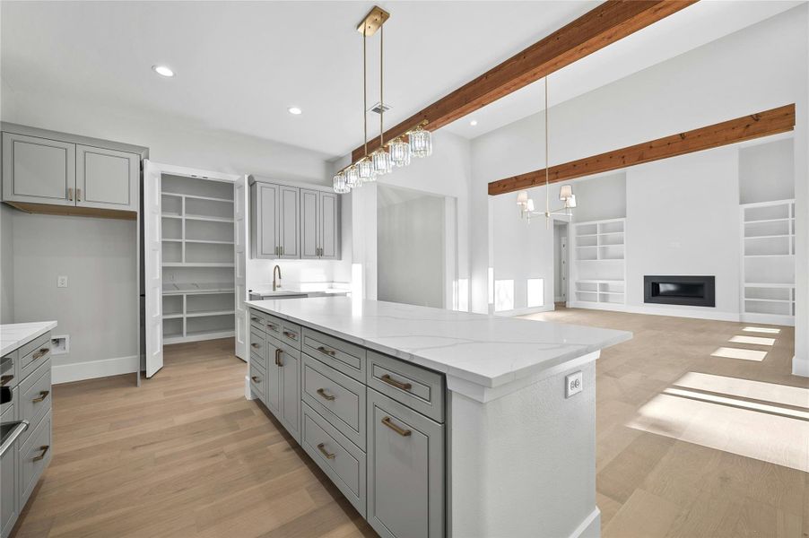 Kitchen with pendant lighting, built in features, gray cabinetry, light stone countertops, and a center island
