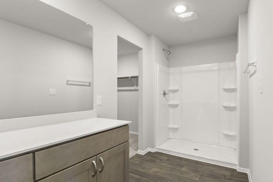 Image of a primary bathroom with brown cabinets, a white double vanity, a large mirror, a vinyl walk-in shower and a walk-in shower