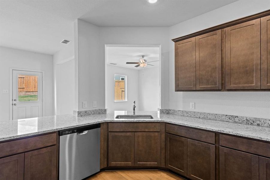 Kitchen with stainless steel dishwasher, light stone counters, dark brown cabinets, light wood finished floors, and ceiling fan Kitchen with stainless steel dishwasher, light stone counters, dark brown cabinets, light wood finished floors, and ceiling fan