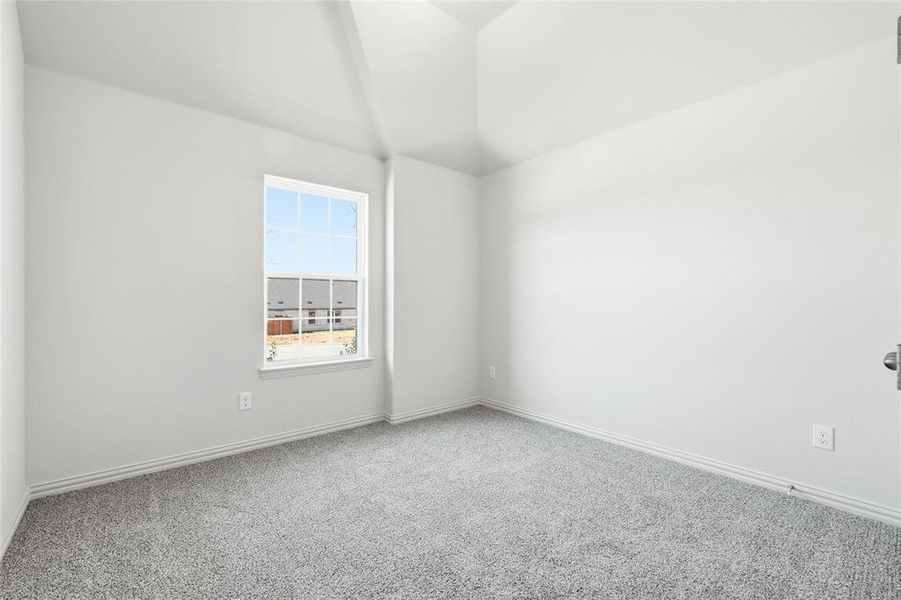 Carpeted spare room featuring vaulted ceiling and baseboards