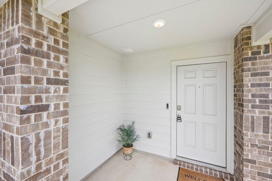 Inviting entryway featuring a paneled white door, brick columns, white horizontal siding, recessed lighting, and concrete flooring