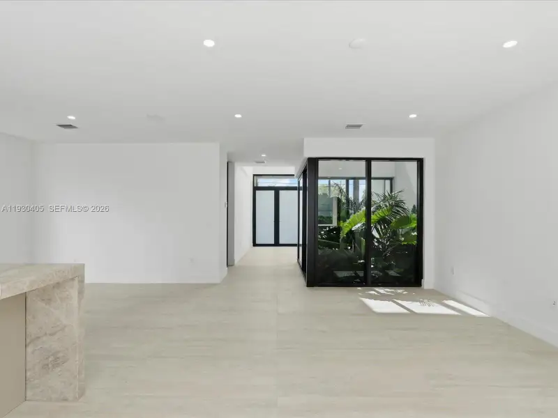 Neutral-toned stone-finish flooring, recessed ceiling lighting, interior glass-paneled garden enclosure with black framing, and stone-clad island feature Neutral-toned stone-finish flooring, recessed ceiling lighting, interior glass-paneled garden enclosure with black framing, and stone-clad island feature