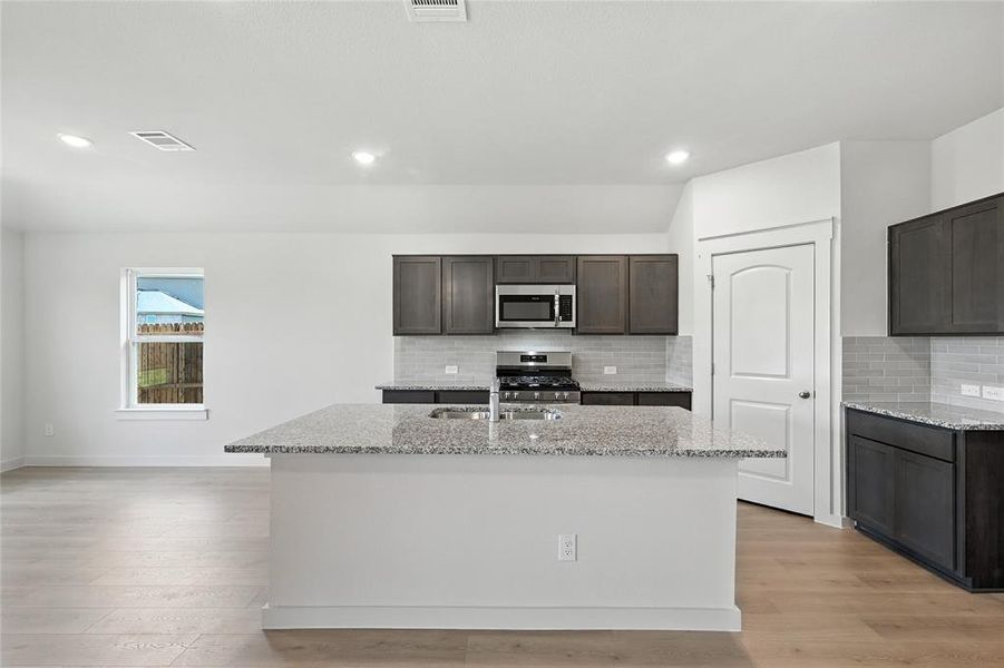 Kitchen with light stone counters, appliances with stainless steel finishes, dark brown cabinetry, light wood-style floors, and recessed lighting Kitchen with light stone counters, appliances with stainless steel finishes, dark brown cabinetry, light wood-style floors, and recessed lighting