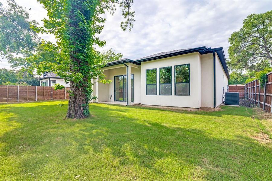 Expansive rear yard featuring a large tree, lush green lawn, and wood privacy fencing