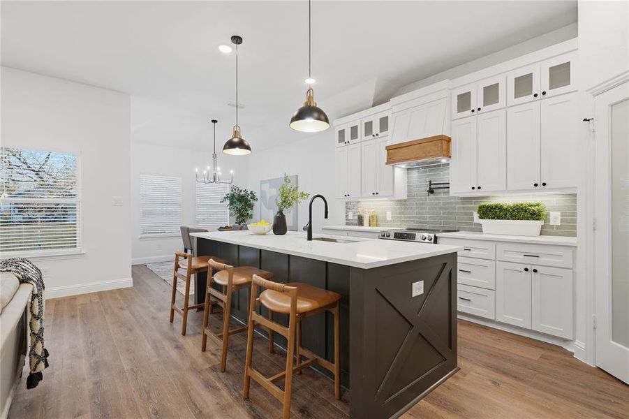 Dual tone kitchen with two tone color scheme, a breakfast bar, a kitchen island with sink, backsplash, and light wood-style floors