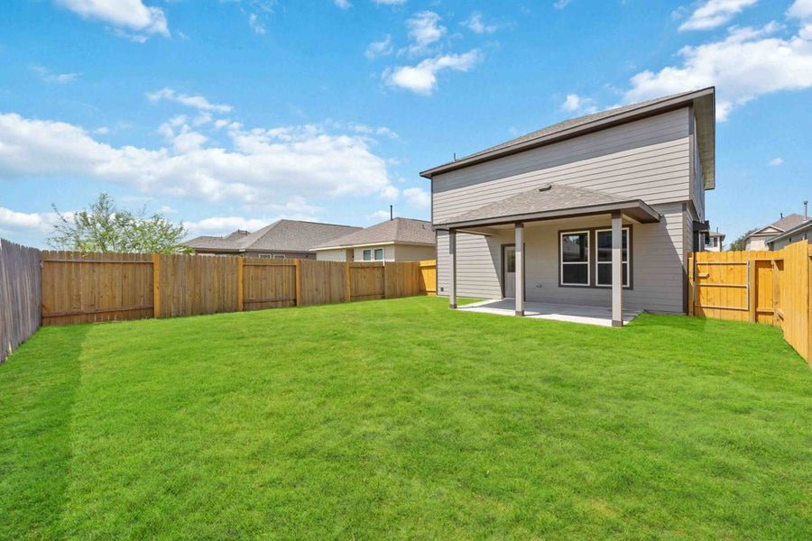 Spacious fenced backyard with green grass and covered patio on two-story home