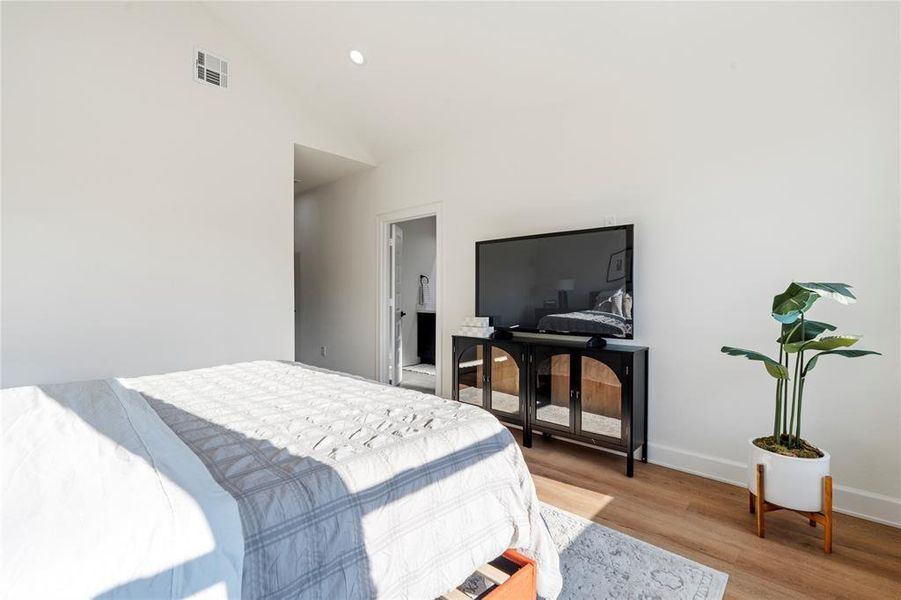 Bright and airy bedroom featuring a large TV on a stylish console, modern decor, and warm wood flooring, complemented by a potted plant for a touch of greenery. Bright and airy bedroom featuring a large TV on a stylish console, modern decor, and warm wood flooring, complemented by a potted plant for a touch of greenery.