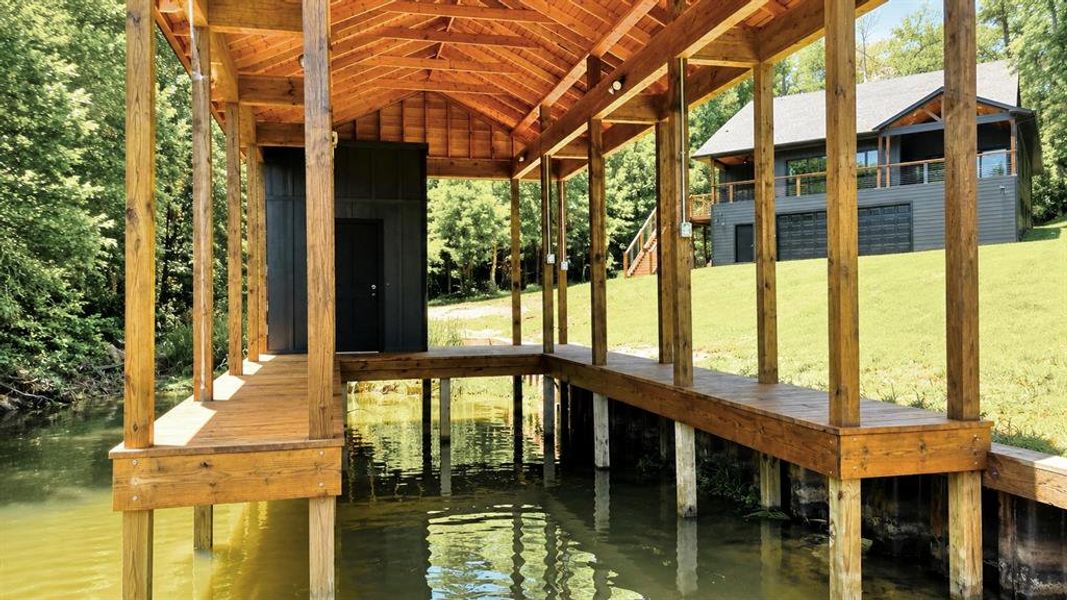 Covered boat dock featuring a wood deck, exposed timber framing, and an enclosed storage area