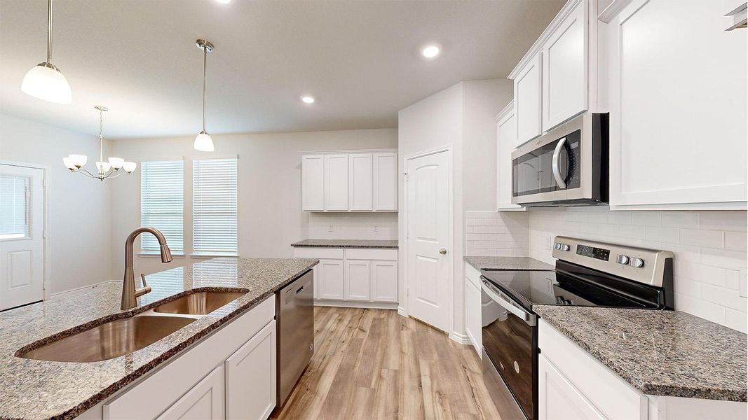 Open-concept kitchen featuring a large island with an undermount double-basin sink and brushed nickel faucet, granite countertops, white cabinetry, and wood-finish flooring Open-concept kitchen featuring a large island with an undermount double-basin sink and brushed nickel faucet, granite countertops, white cabinetry, and wood-finish flooring