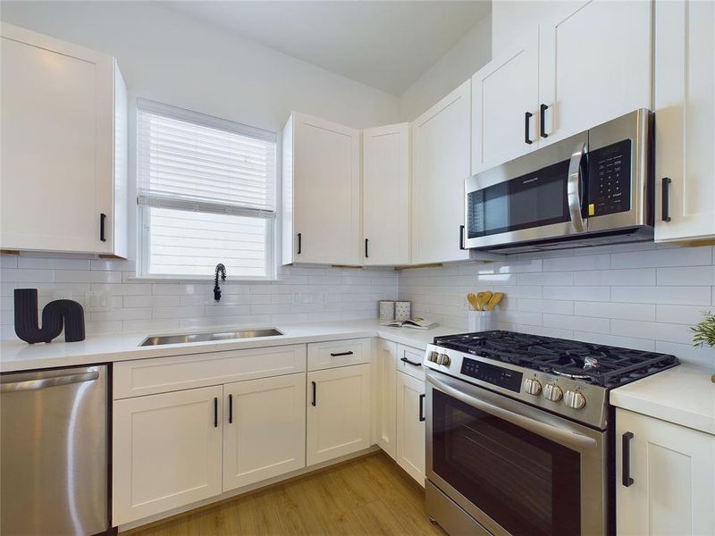 kitchen featuring white shaker cabinets, sleek black hardware, subway tile backsplash, and quartz countertops. It's equipped with a deep sink and has ample storage space.