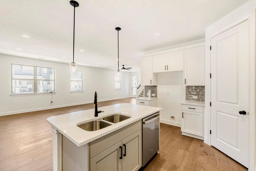 Kitchen featuring tasteful backsplash, light wood finished floors, open floor plan, an island with sink, and stainless steel dishwasher Kitchen featuring tasteful backsplash, light wood finished floors, open floor plan, an island with sink, and stainless steel dishwasher