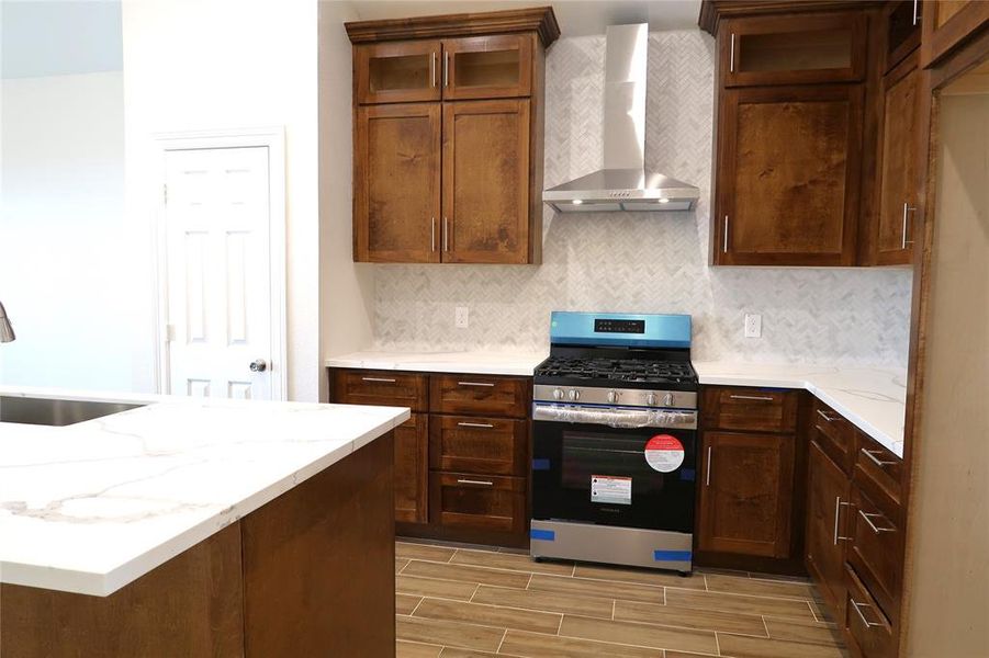 Stainless steel appliances and hood with tile backsplash throughout kitchen.