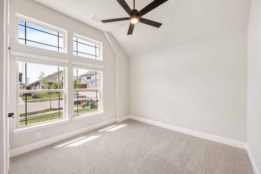 Empty bedroom with vaulted ceiling, ceiling fan, carpet flooring, and large windows overlooking a neighborhood street. Empty bedroom with vaulted ceiling, ceiling fan, carpet flooring, and large windows overlooking a neighborhood street.