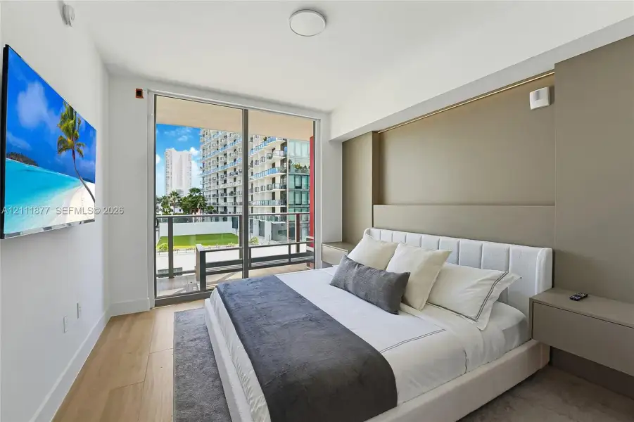 Wood-finish flooring, floor-to-ceiling glass sliding door, balcony access, and built-in bedside shelving