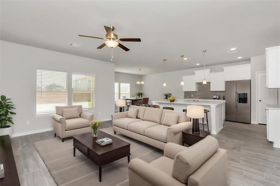 Discover the beauty of open-concept living in this expansive space that effortlessly blends the living room, dining area, and kitchen. The layout is designed to foster connection, with modern pendant lighting illuminating the sleek, white kitchen, complete with stainless steel appliances and a spacious breakfast bar. This harmonious flow from one area to another makes it an entertainer's dream. **This image is from another Saratoga Home with similar floor plan and finishes, not the June floorplan.**