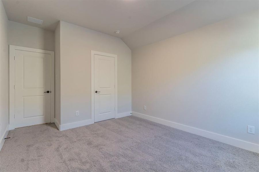 Unfurnished bedroom featuring light carpet and lofted ceiling