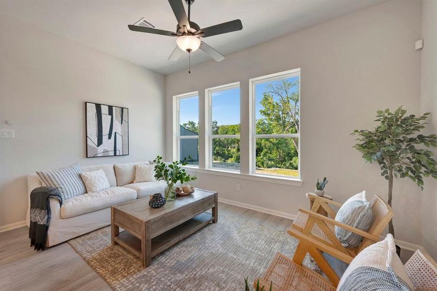 Bright living area featuring wood-finish flooring, a contemporary ceiling fan, and three large windows