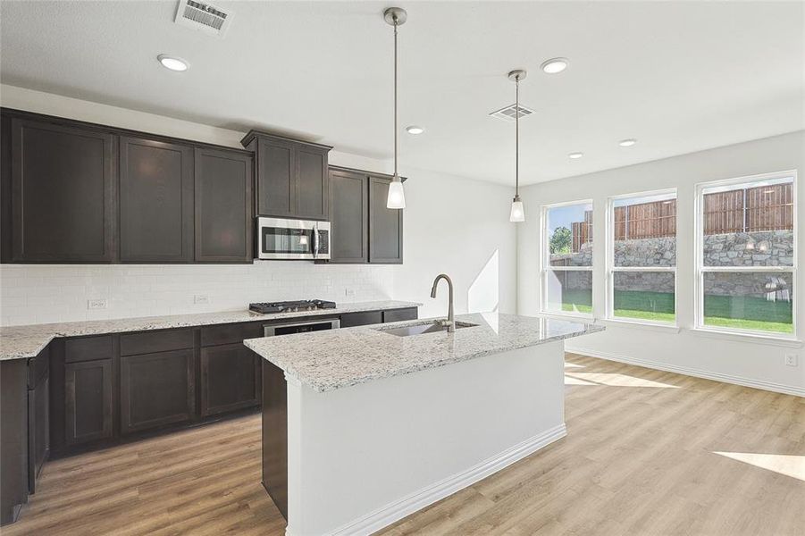 Kitchen featuring light hardwood / wood-style flooring, tasteful backsplash, light stone countertops, appliances with stainless steel finishes, and sink