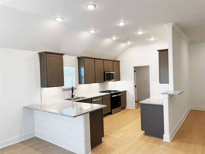 Kitchen featuring a peninsula, a sink, tasteful backsplash, light stone counters, and appliances with stainless steel finishes