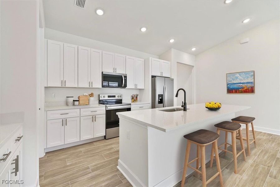 Kitchen featuring stainless steel appliances, wood finish floors, a breakfast bar area, a kitchen island with sink, and white cabinets