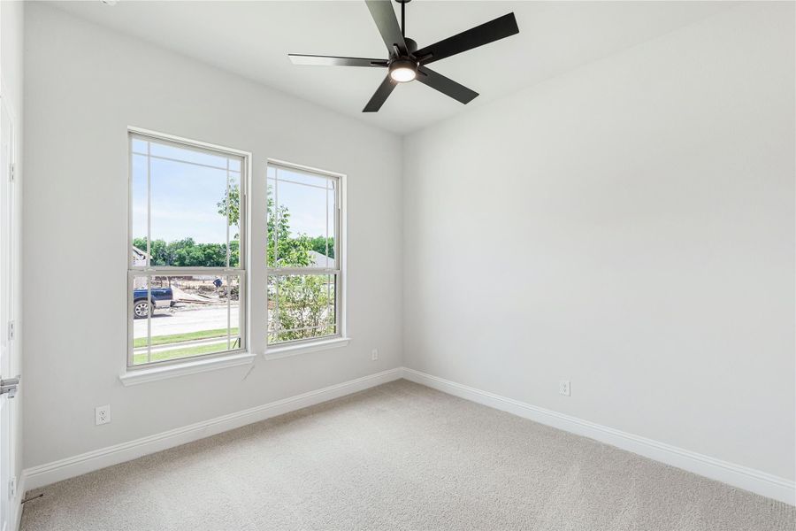 Empty bedroom with carpet flooring, two windows, and a black ceiling fan with light