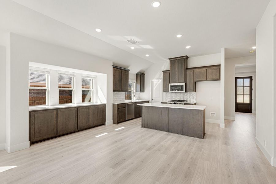 Open kitchen with dark brown cabinets, center island, white countertops, and light hardwood floors