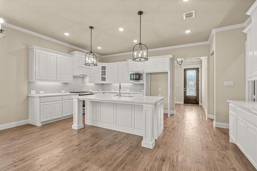 Kitchen featuring light wood-type flooring, appliances with stainless steel finishes, decorative backsplash, and white cabinetry