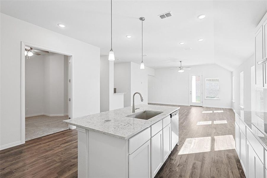 Kitchen featuring decorative light fixtures, white cabinetry, sink, and an island with sink