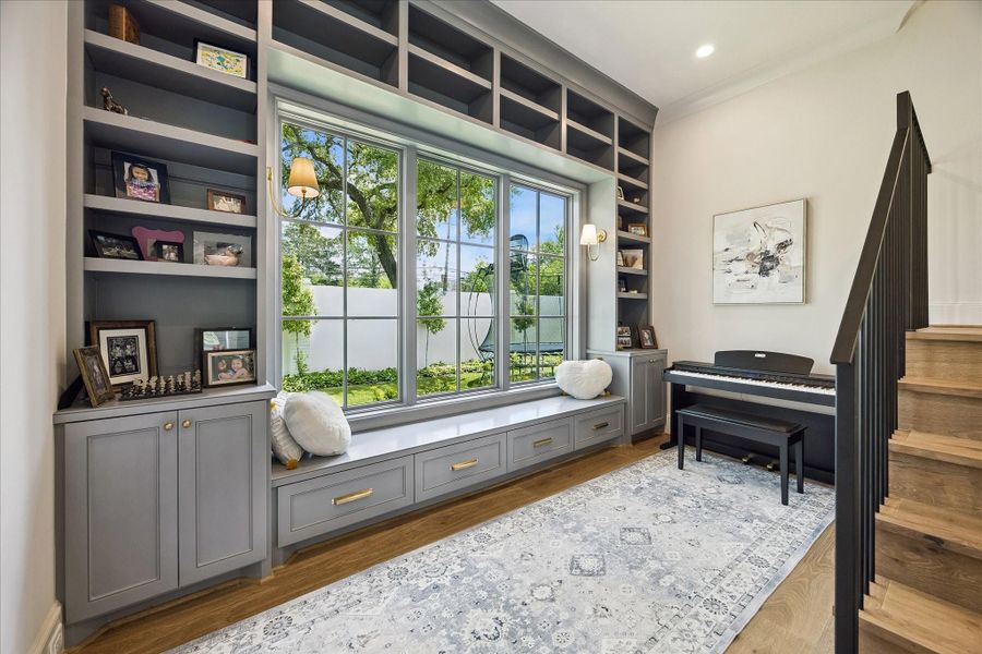 Inviting flex space featuring a wall of custom built-in cabinetry and shelving framing a large divided light picture window, creating a bright, functional setting ideal for music, reading or relaxation. A built-in window seat offers additional seating and storage, while wall sconces provide warm accent lighting.