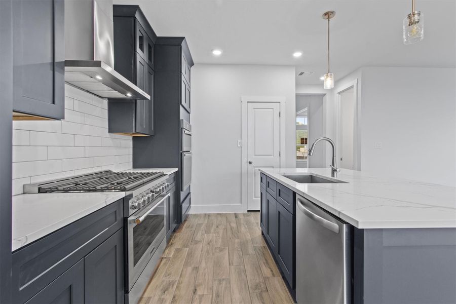 Kitchen with tasteful backsplash, appliances with stainless steel finishes, wall chimney exhaust hood, and pendant lighting