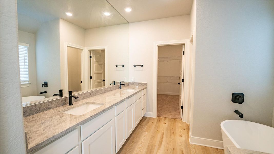 Full bathroom with double vanity, a freestanding tub, light wood-style flooring, recessed lighting, and a walk in closet Full bathroom with double vanity, a freestanding tub, light wood-style flooring, recessed lighting, and a walk in closet