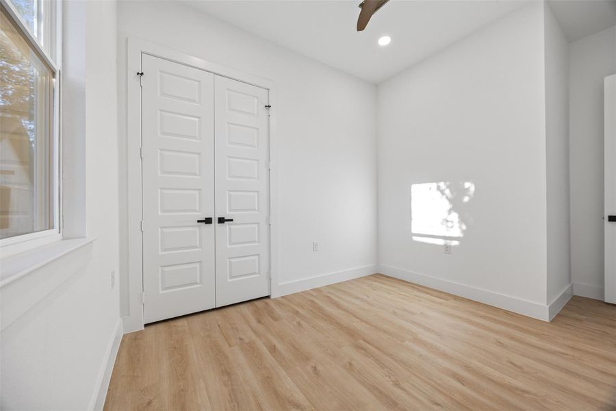 Bright room with light wood-like flooring, white walls, and double doors. A window allows natural light, creating a spacious and airy feel.