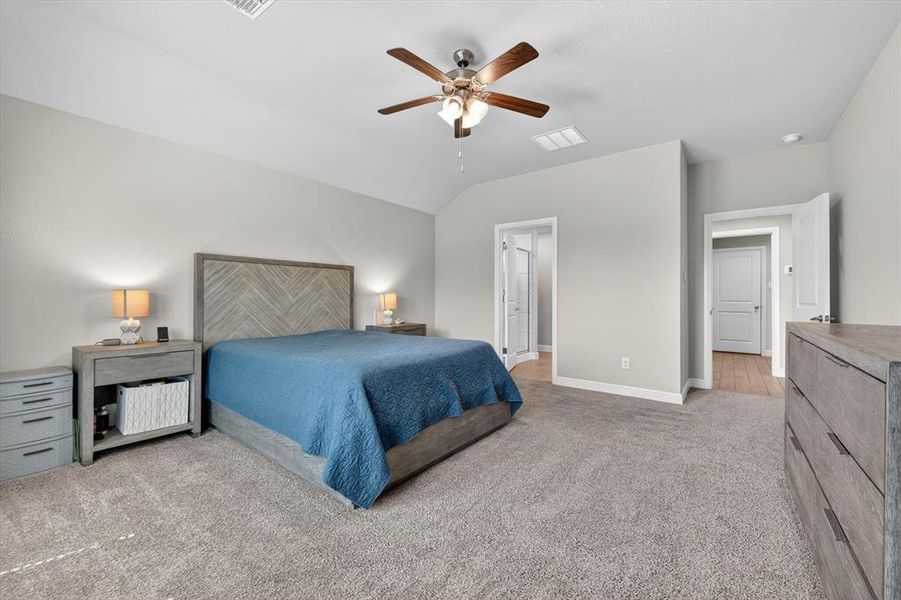 Spacious bedroom featuring plush carpeting, a vaulted ceiling, and a ceiling fan with integrated lighting