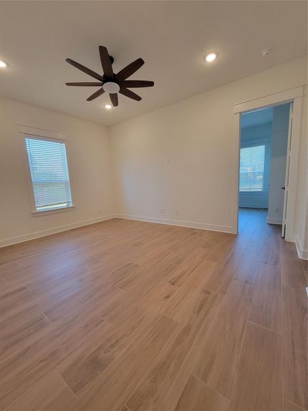 This room features light wood-look tile flooring, a modern ceiling fan, and recessed lighting. It has neutral walls with a large window for natural light and an open doorway leading to another space. This room features light wood-look tile flooring, a modern ceiling fan, and recessed lighting. It has neutral walls with a large window for natural light and an open doorway leading to another space.