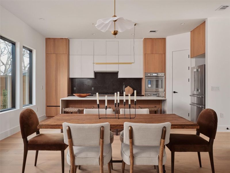 Two tone kitchen with light wood-type flooring, modern cabinets, stainless steel appliances, light countertops, and two tone cabinets