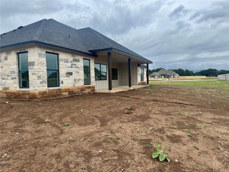 A newly constructed residence showcases a charming stone and siding exterior with a covered patio, ready for personalized landscaping.