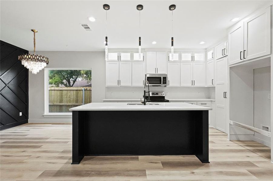 Kitchen with an island with sink, light hardwood / wood-style floors, pendant lighting, white cabinets, and appliances with stainless steel finishes