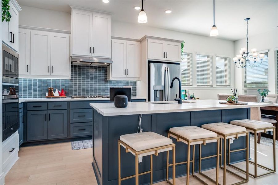 Kitchen with two tone cabinetry, an island with sink, stainless steel appliances, a kitchen breakfast bar, and light wood finished floors
