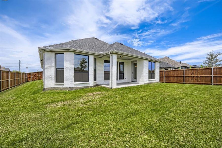 Expansive backyard featuring a manicured lawn, full wood fencing, and a covered concrete patio