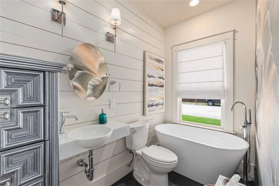 Bathroom featuring white shiplap walls, a freestanding soaking tub, a vessel sink with a wall-mounted countertop, and chrome fixtures