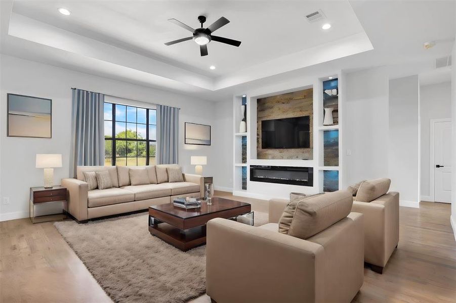 Living room with ceiling fan, a raised ceiling, and light hardwood / wood-style floors