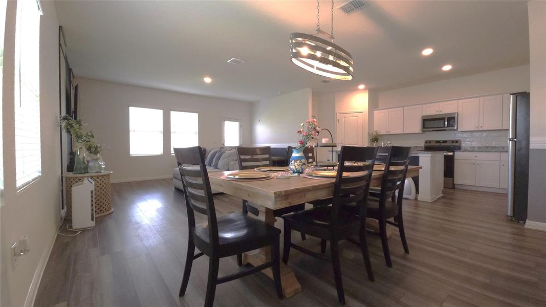 Spacious dining area with wood-finish flooring, featuring a modern chandelier and recessed lighting