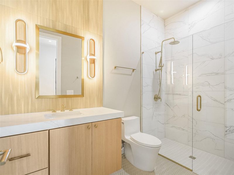The bathroom features a modern vanity with a white countertop and light wood cabinetry, a gold-framed mirror, and contemporary sconce lighting