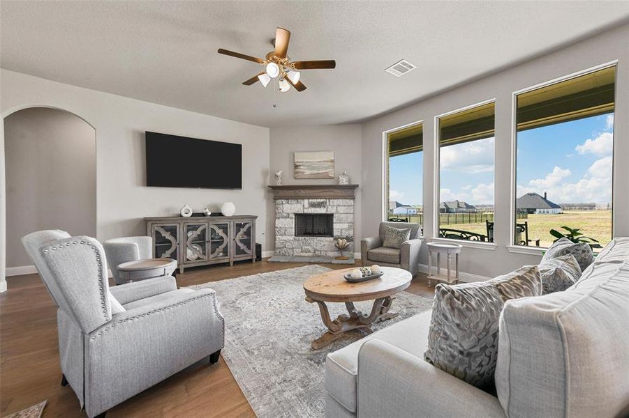 Living room with a stone fireplace, ceiling fan, and dark wood-type flooring