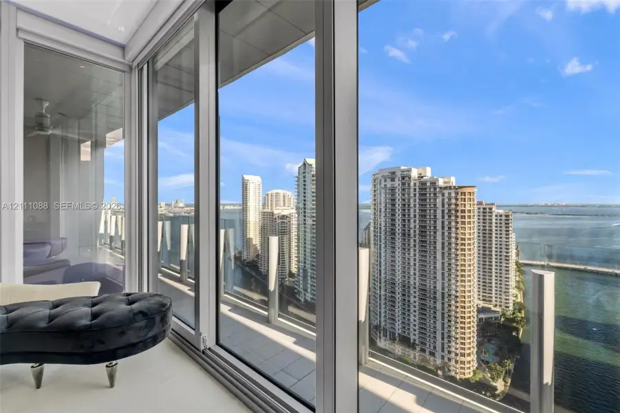 Floor-to-ceiling glass paneling, metal-frame sliding doors, expansive balcony featuring a glass balustrade, and high-rise cityscape and water scenery Floor-to-ceiling glass paneling, metal-frame sliding doors, expansive balcony featuring a glass balustrade, and high-rise cityscape and water scenery