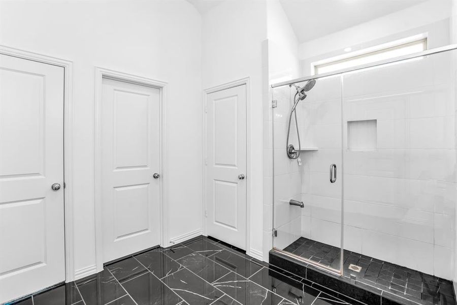 Glass-enclosed shower featuring a handheld showerhead, built-in shelving, and a tiled bench