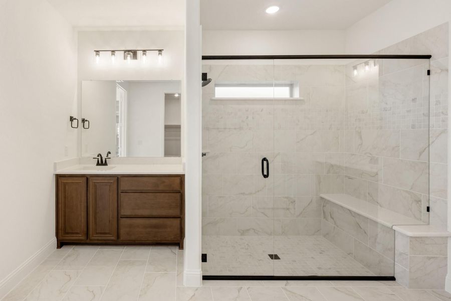 Bathroom with wood vanity, large mirror, and glass-enclosed marble tile shower with built-in bench