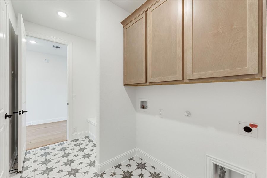 Laundry room with light wood upper cabinets, washer and dryer hookups, and patterned tile floor
