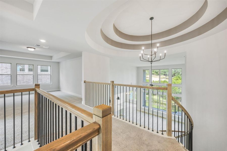 Corridor featuring a tray ceiling, carpet floors, plenty of natural light, and an upstairs landing