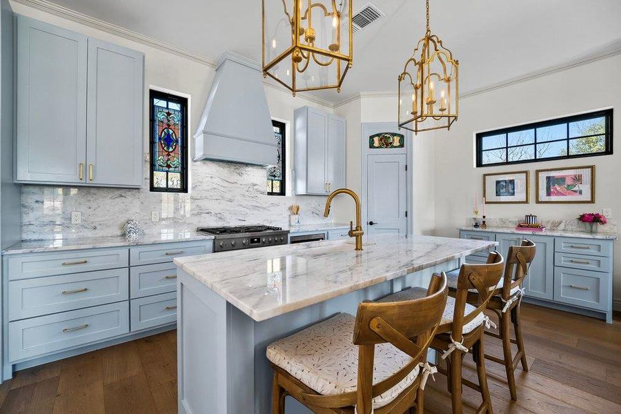 Kitchen with light stone countertops, decorative backsplash, a center island with sink, dark wood finished floors, and ornamental molding